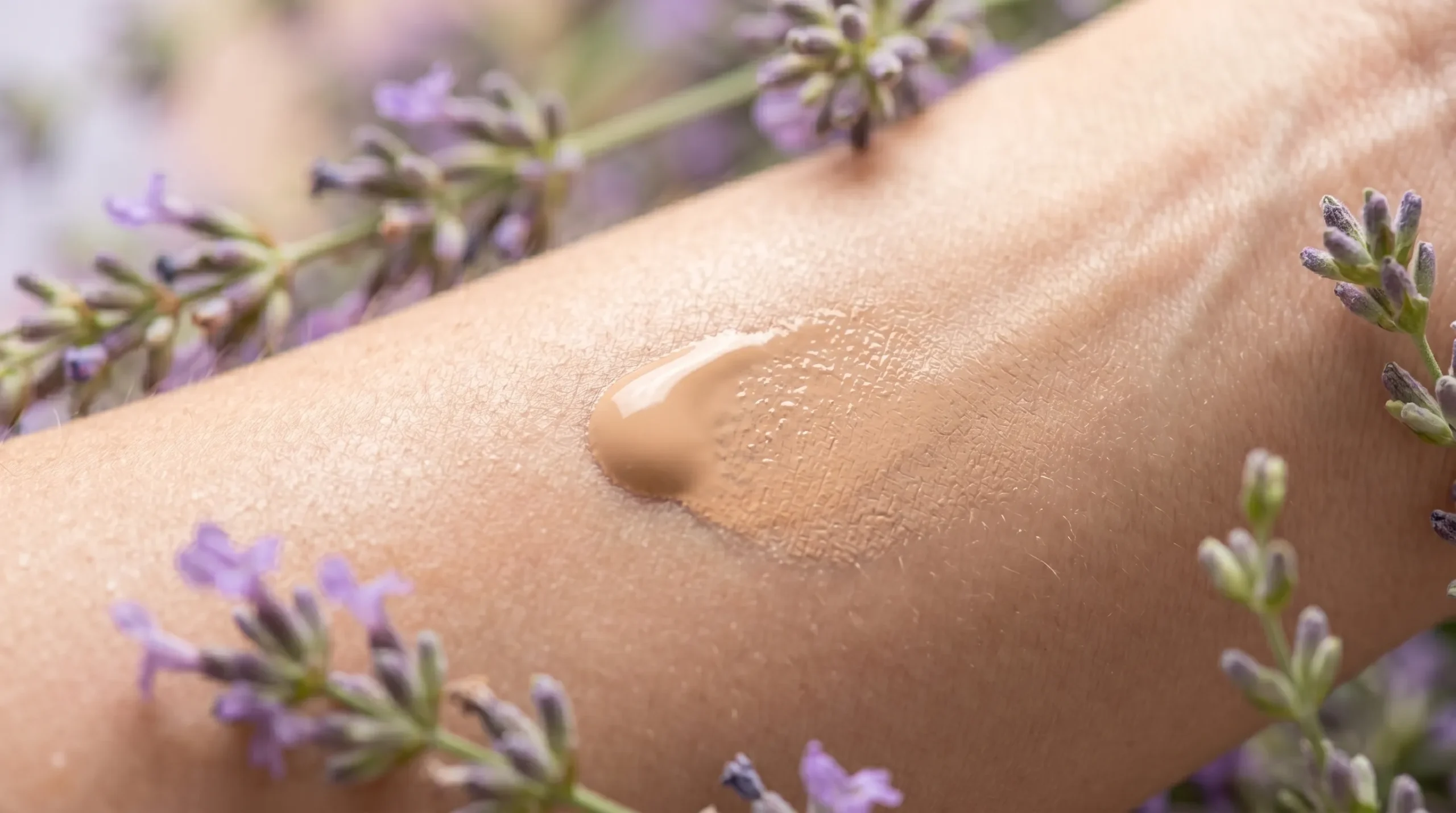 Gota de base de maquiagem orgânica sendo aplicada suavemente em uma pele saudável, cercada por flores de lavanda